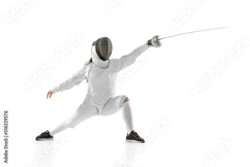 Young girl, beginner fencer in fencing costume and mask practicing with rapier isolated on white background. Sport, youth, healthy lifestyle, achievements.