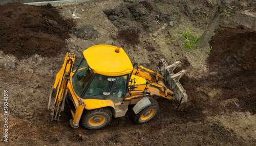 yellow construction excavator throws the earth onto a flower bed,
