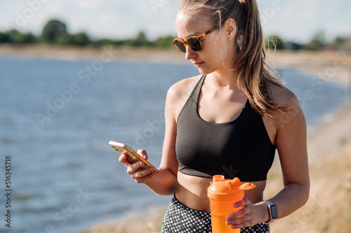 Sporty woman in sportsuit walking down the lake and using a cellphone photo