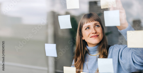 Young female entrepreneur sticking adhesive notes to a glass wall photo