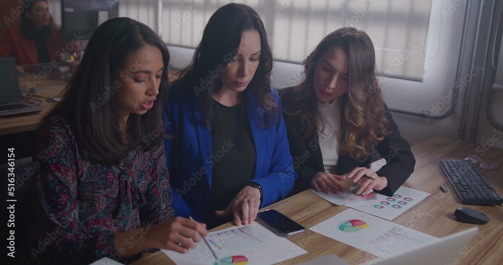 Fototapeta premium A senior business woman explaining results to female staff showing graphs and statistics. Business female leader explaining corporate life