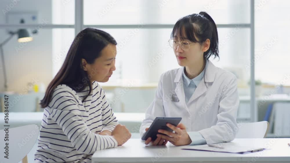 Asian female doctor explaining woman treatments plan on digital tablet while giving consultation in clinic Asian female doctor explaining woman treatments plan on digital tablet while giving consultation in clinic