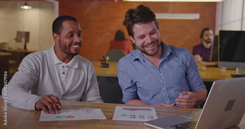 Two diverse millennial employees in front of laptop. A black colleague explains new job for a south American female employee. First day at new job concept Two diverse millennial employees in front of laptop. A black colleague explains new job for a south American female employee. First day at new job concept