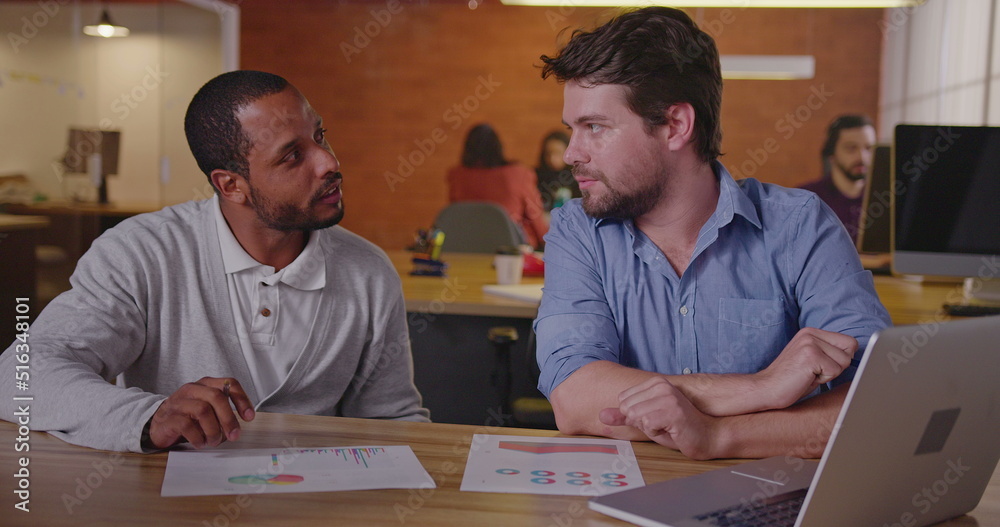 Two diverse millennial employees in front of laptop. A black colleague explains new job for a south American female employee. First day at new job concept Two diverse millennial employees in front of laptop. A black colleague explains new job for a south American female employee. First day at new job concept