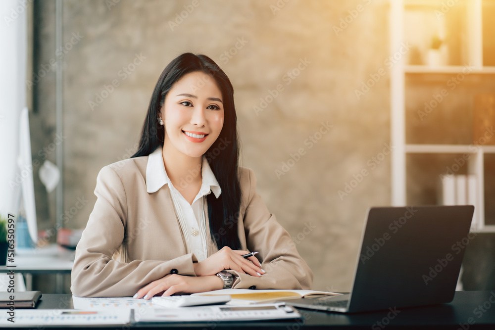 Portrait of attractive woman sitting at office desk, writing on notebook and looking at laptop screen