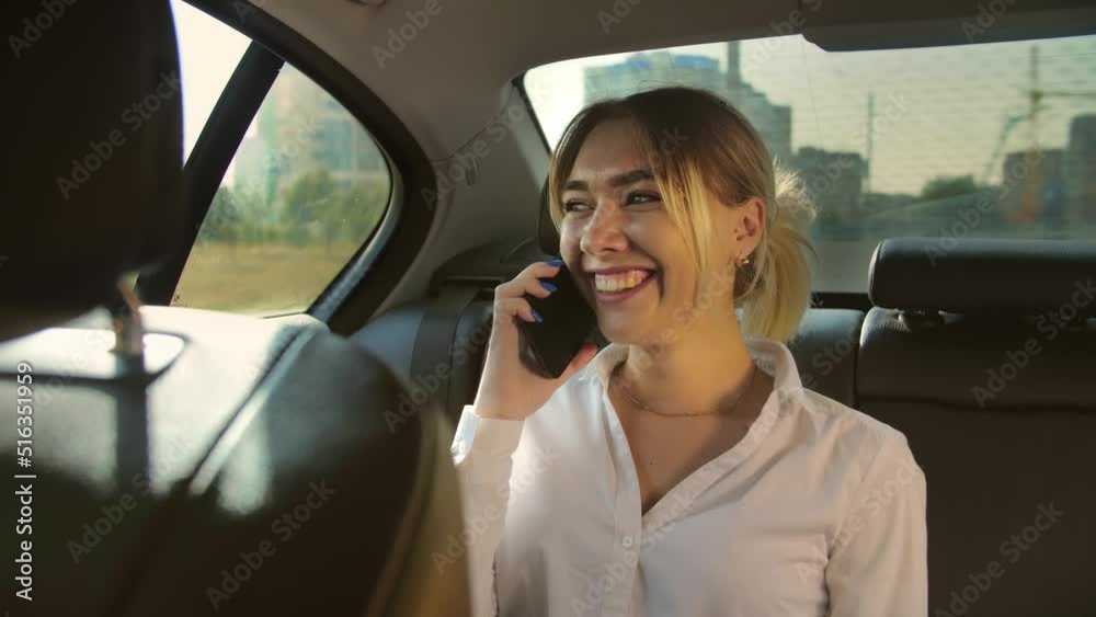 Attractive young woman in a business suit talking on the phone on back seat car.Business woman holding smartphone and smiling.Riding car and talking woman. Attractive young woman in a business suit talking on the phone on back seat car.Business woman holding smartphone and smiling.Riding car and talking woman.
