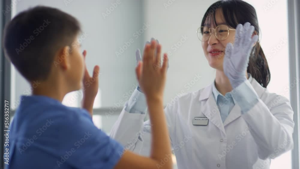 Cheerful Asian female doctor and tween boy talking and high fiving each other after medical checkup in clinic Cheerful Asian female doctor and tween boy talking and high fiving each other after medical checkup in clinic