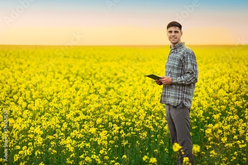 Farmer business man in colza rapeseed field  with digital tablet computer. Agricultural concept. Harvest in field in summer.