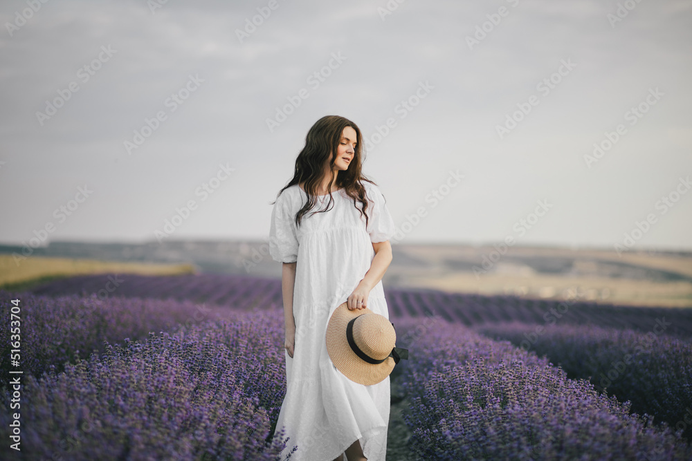 Young beautiful woman in white dress enjoying fragrance of lavender field.