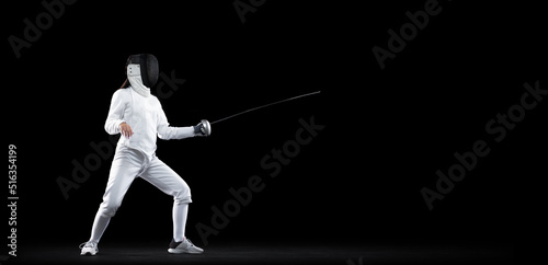 Sportive girl, female fencer in white fencing costume and mask in action, motion isolated on dark background. Sport, youth, activity, skills, achievements, goal. © master1305