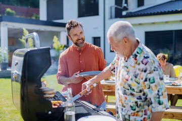 Senior father with adult son grilling outside on backyard in summer family during garden party