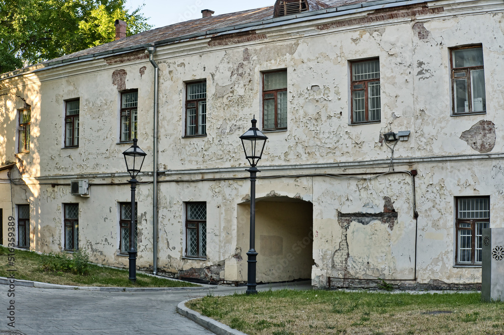 The fragment of the old building facade. Cracks on the plaster and broken windows. Emergency residential building. Old two-story house with an arch.