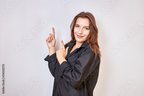 A beautiful girl in a black shirt shows a gesture pointing upwards with the fingers of both hands.