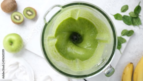 Green vegan smoothie blending in electric blender cup, slow motion, top view. Preparation of detox green smoothie juice