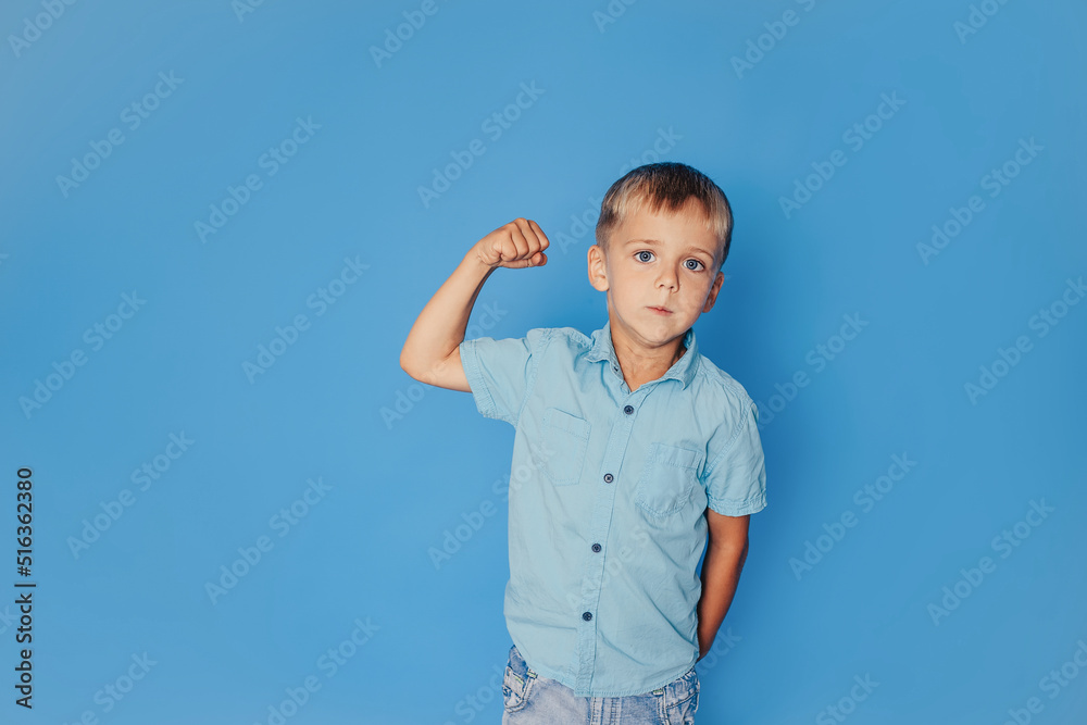 The concept of childhood, power, strength and people is a happy smiling boy in showing strong fists on a blue background The concept of childhood, power, strength and people is a happy smiling boy in showing strong fists on a blue background