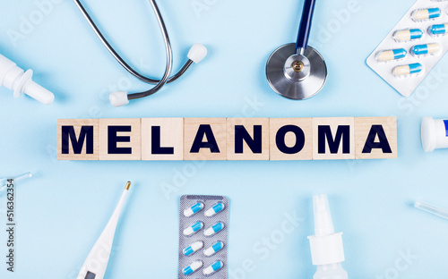 On a blue background, a stethoscope, a thermometer, other medicines and wooden cubes with the text MELANOMA. View from above. Medical concept