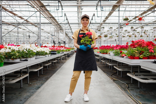 Pretty female gardener holding potted plant in greenhouse