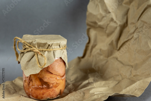 A glass jar of canned meat. Homemade stew in front of the gray background. Slices of appetizing meat tightly packed in a transparent jar. Food ready to eat. Close-up. Selective focus.