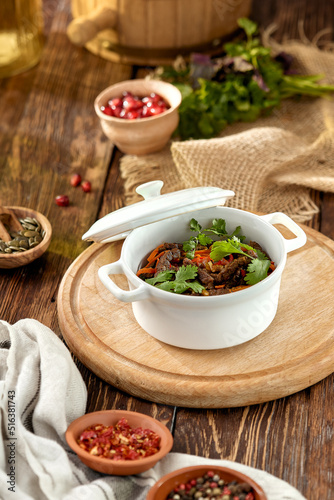 Beef ragout with vegetables in ceramic pot on wooden rustic background. Stew meat with coriander leaf on casserole in georgian style. Composition with meat ragout on wooden table with ingredients.