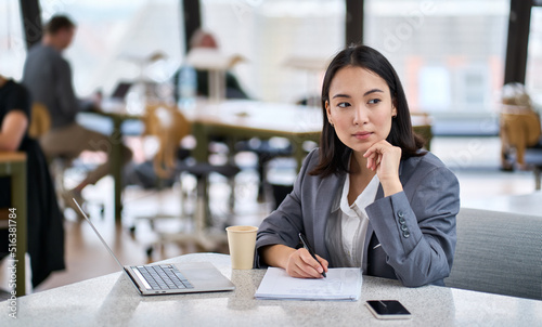 Fotografie Young thoughtful Asian business woman executive manager wearing suit working in modern office, taking notes and thinking of professional plan, project management, considering new business ideas