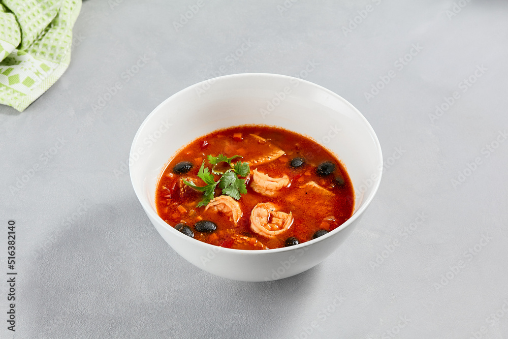 Fish tomato soup with shrimps and black olives. Seafood soup with prawns in white ceramic bowl on concrete background. Fish dish with seafood. Tomato soup in minimal composition. Fish tomato soup with shrimps and black olives. Seafood soup with prawns in white ceramic bowl on concrete background. Fish dish with seafood. Tomato soup in minimal composition.