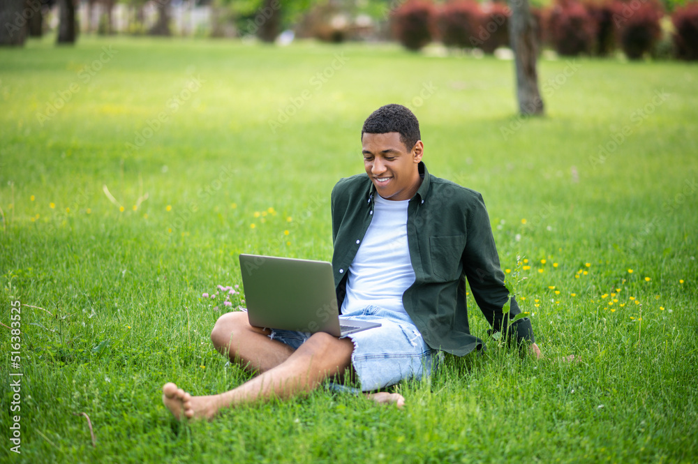 Guy looking with interest at laptop sitting on grass Guy looking with interest at laptop sitting on grass