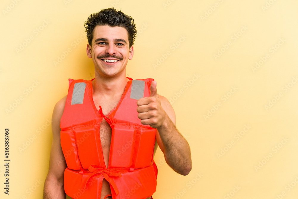 Young caucasian man wearing life jacket isolated on yellow background smiling and raising thumb up Young caucasian man wearing life jacket isolated on yellow background smiling and raising thumb up