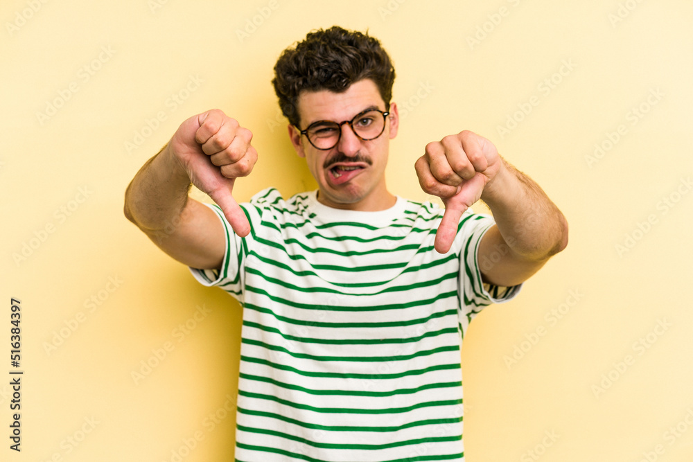 Fototapeta premium Young caucasian man isolated on yellow background showing thumb down and expressing dislike.