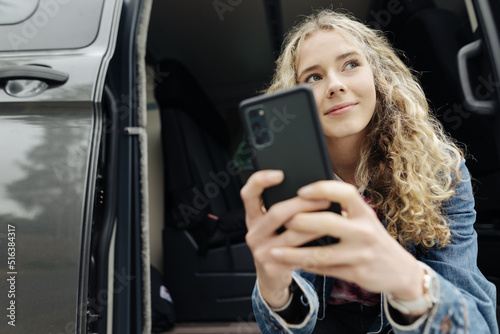 Young teenager sitting with her cell phone in camping van and looking to the side