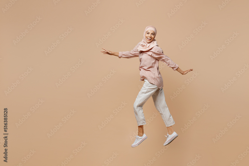 Full size young fun arabian asian muslim woman she wear abaya hijab pink clothes jump high with outstretched hands isolated on plain pastel light beige background People uae islam religious concept