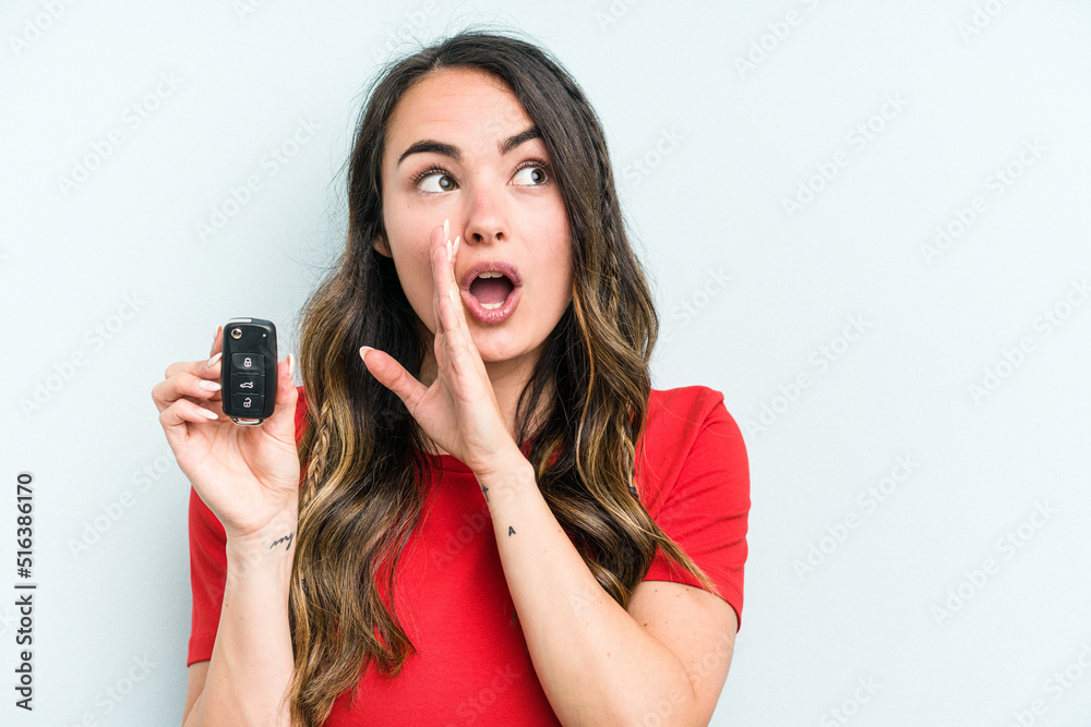 Young caucasian woman holding car keys isolated on blue background is saying a secret hot braking news and looking aside Young caucasian woman holding car keys isolated on blue background is saying a secret hot braking news and looking aside