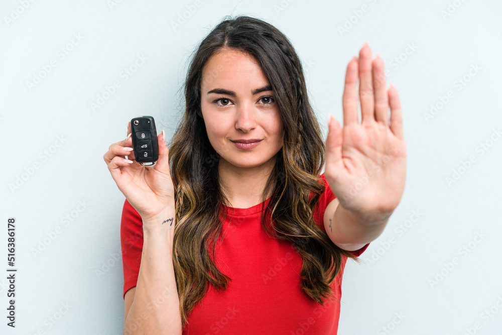 Young caucasian woman holding car keys isolated on blue background standing with outstretched hand showing stop sign, preventing you. Young caucasian woman holding car keys isolated on blue background standing with outstretched hand showing stop sign, preventing you.