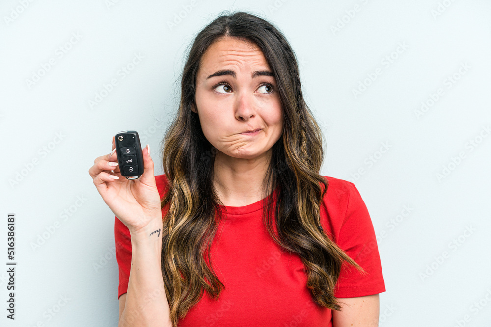 Young caucasian woman holding car keys isolated on blue background confused, feels doubtful and unsure. Young caucasian woman holding car keys isolated on blue background confused, feels doubtful and unsure.