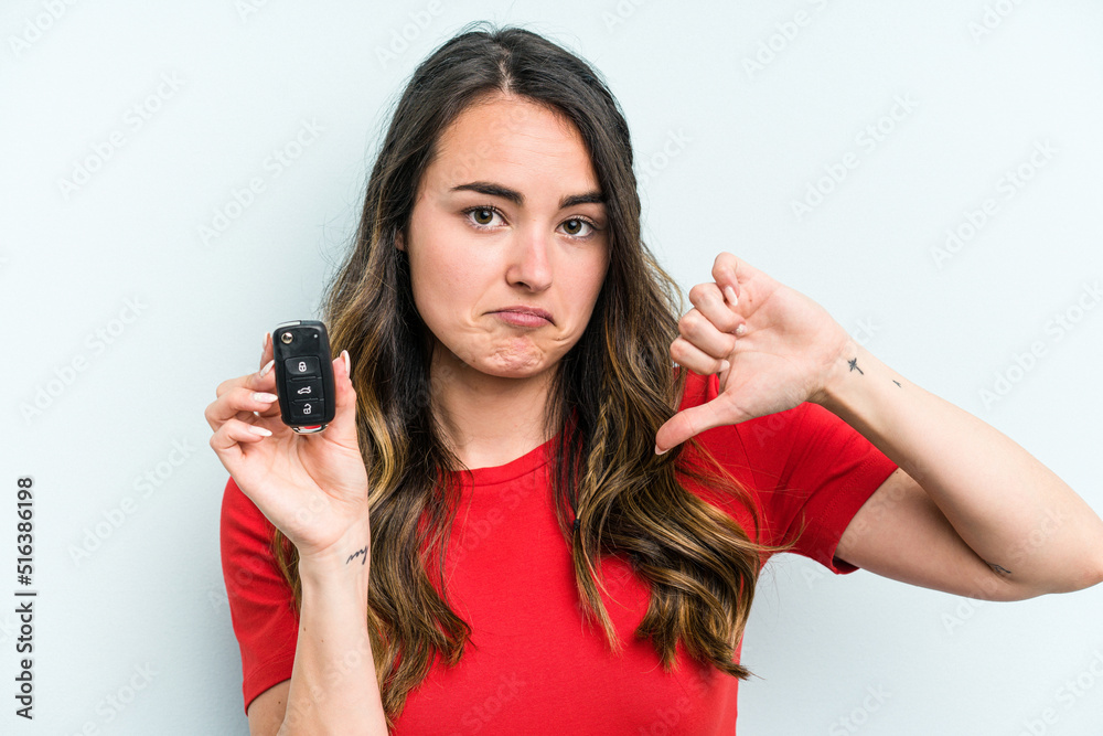 Young caucasian woman holding car keys isolated on blue background showing a dislike gesture, thumbs down. Disagreement concept. Young caucasian woman holding car keys isolated on blue background showing a dislike gesture, thumbs down. Disagreement concept.