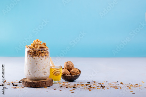 Overnight oats with walnuts, accompanied with honey and whole walnuts. Photo with a blue background and space to add text. Cinnamon powder, oatmeal, and cloves are scattered on the surface.