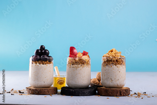 Three Overnight oats with walnuts, apple fruits, and black grapes fruits. Honey and whole walnuts. Photo with a blue background and space to add text. Cinnamon, oatmeal, and cloves on the surface.