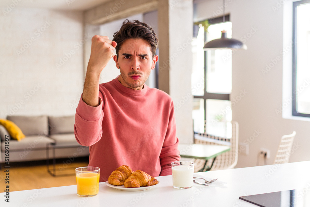 Young mixed race man having breakfast in a kitchen on the morning showing fist to camera, aggressive facial expression. Young mixed race man having breakfast in a kitchen on the morning showing fist to camera, aggressive facial expression.