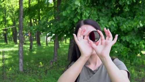 The girl holds an ND filter in her hands and looks through it with one eye and slowly twists it, the filter turns black
