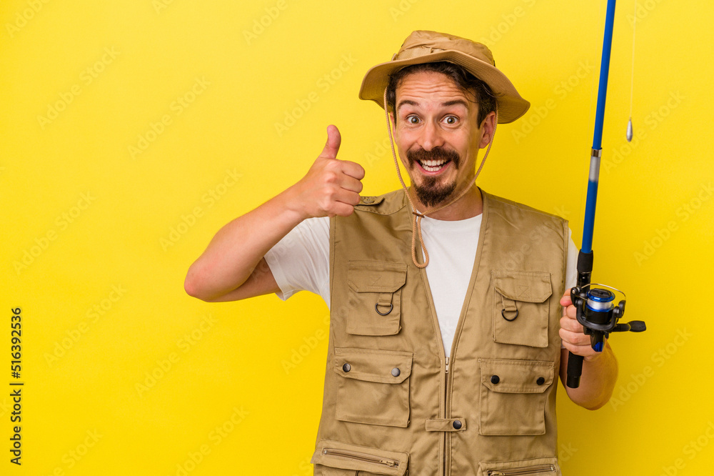 Young caucasian fisherman holding rod isolated on yellow background smiling and raising thumb up Young caucasian fisherman holding rod isolated on yellow background smiling and raising thumb up