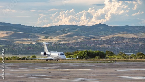 White business jet with turbofan engines on the airport with attractive panoramic mountain landscape and cloudy sky. Modern technology in fast transportation, business travel and tourism, aviation. photo