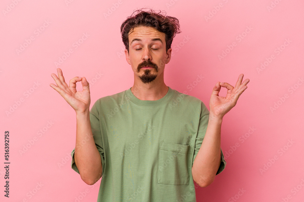 Young caucasian man isolated on pink background relaxes after hard working day, she is performing yoga.
