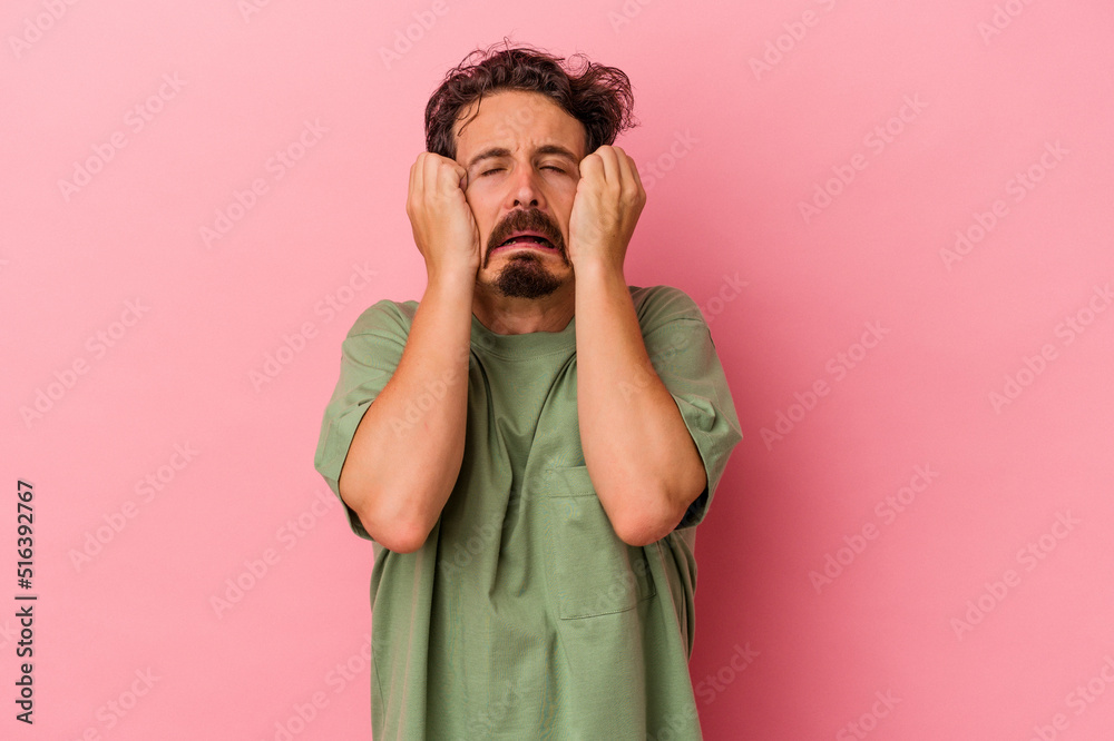 Young caucasian man isolated on pink background crying, unhappy with something, agony and confusion concept. Young caucasian man isolated on pink background crying, unhappy with something, agony and confusion concept.