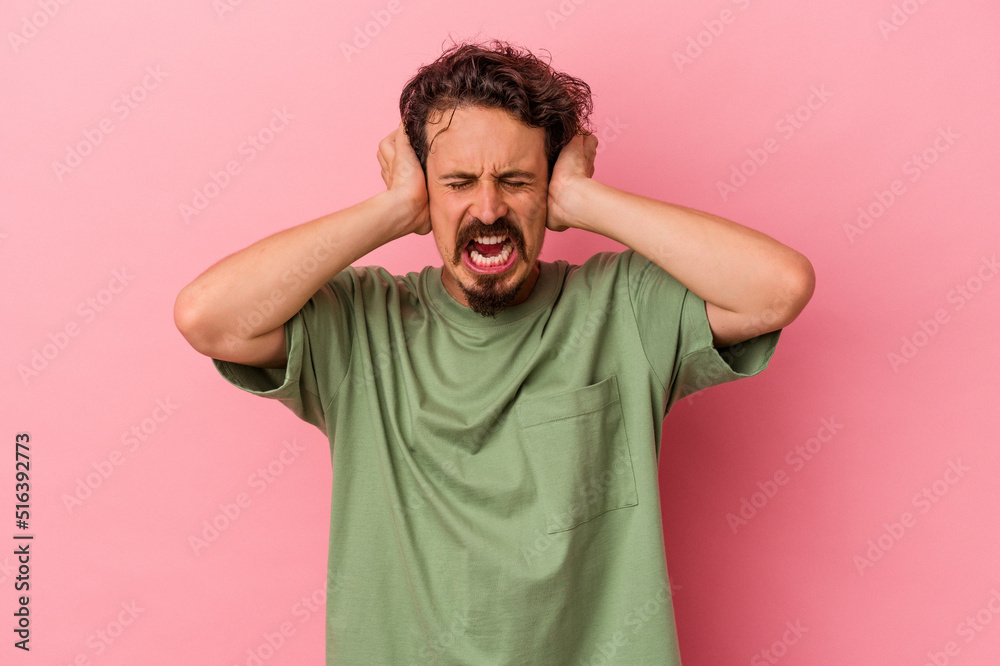 Young caucasian man isolated on pink background covering ears with hands trying not to hear too loud sound. Young caucasian man isolated on pink background covering ears with hands trying not to hear too loud sound.