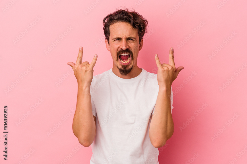 Young caucasian man isolated on pink background showing a horns gesture as a revolution concept. Young caucasian man isolated on pink background showing a horns gesture as a revolution concept.