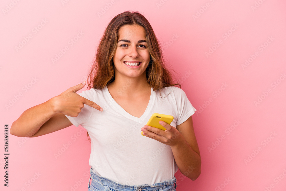 Young caucasian woman using mobile phone isolated on pink background person pointing by hand to a shirt copy space, proud and confident Young caucasian woman using mobile phone isolated on pink background person pointing by hand to a shirt copy space, proud and confident