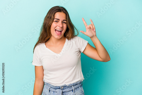 Young caucasian woman isolated on blue background  showing a horns gesture as a revolution concept.