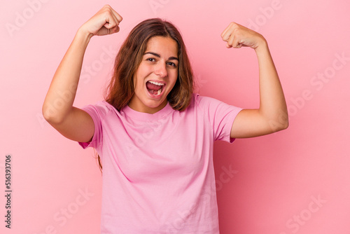 Young caucasian woman isolated on pink background  showing strength gesture with arms, symbol of feminine power © Asier
