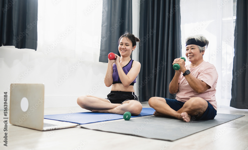 Obraz premium Home workout concept, Asian woman and Asian old woman exercising and lifting dumbbells according to video guide in laptop.