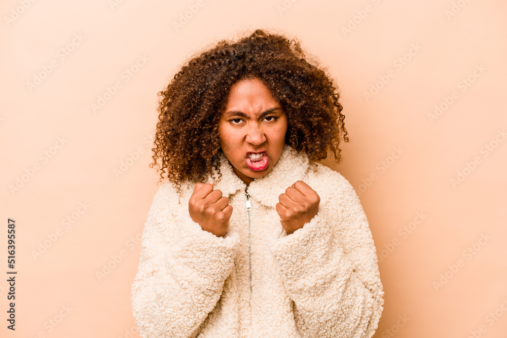 Young African American woman isolated on beige background showing fist to camera, aggressive facial expression. Young African American woman isolated on beige background showing fist to camera, aggressive facial expression.