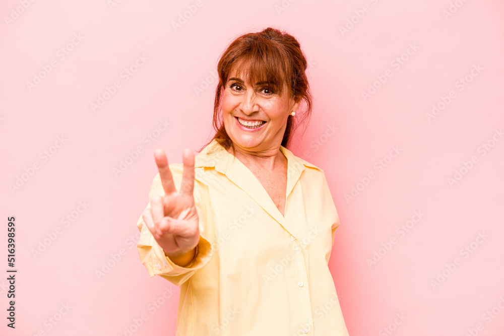 Fototapeta premium Middle age caucasian woman isolated on pink background joyful and carefree showing a peace symbol with fingers.